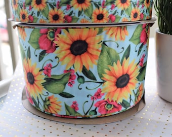 Puede incluir: Un rollo de cinta azul y blanca con un estampado floral de girasoles y amapolas. La cinta está envuelta alrededor de un tubo de cartón.