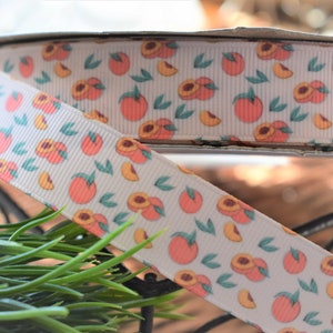 May include: White ribbon with a peach print. The ribbon has a repeating pattern of peaches and leaves.
