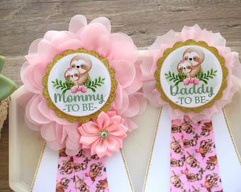May include: Two pink and gold sashes with sloth designs. One sash says "Mommy-to-be" and the other says "Daddy-to-be".