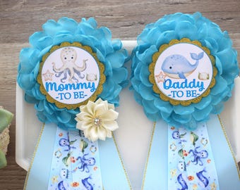 May include: Two blue and gold sashes with a flower accent. One sash says "Mommy-to-be" with an octopus illustration. The other sash says "Daddy-to-be" with a whale illustration.
