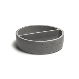 Könnte beinhalten: Eine geteilte Schale aus grauem Beton mit runder Form. Die Schale hat eine glatte, strukturierte Oberfläche und ist in zwei Abschnitte unterteilt.
