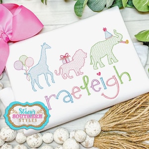 May include: A white embroidered shirt with a giraffe, lion, elephant, and balloons. The name "raeleigh" is embroidered in colorful letters.