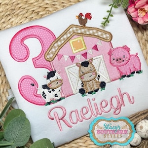 May include: Pink and white embroidered design of a barn with animals, including a pig, cow, and horse. The design also includes a number "3" and the name "Raeleigh".