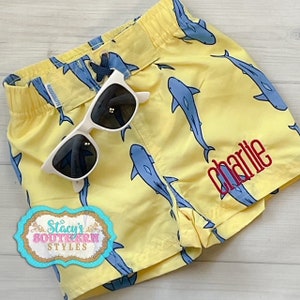 Può includere: Costume da bagno giallo con motivo a squalo blu e il nome "Charlie" ricamato in rosso.