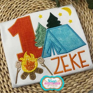 K&ouml;nnte beinhalten: Wei&szlig;es T-Shirt mit Camping-Motiv. Mit einer gro&szlig;en orangefarbenen Zahl 1, einem blauen Zelt, B&auml;umen, einem Lagerfeuer mit Marshmallows und dem Namen "ZEKE" in Orange. Enth&auml;lt ein Logo mit der Aufschrift "Stacy's Southern Styles".