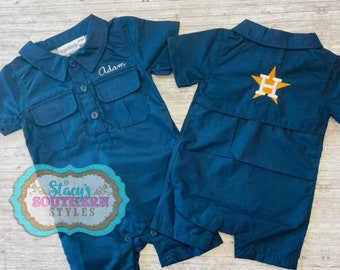 May include: Two teal blue baby onesies. One has the name "Adam" embroidered on the front. The other has a yellow star with a white "H" in the center on the back.