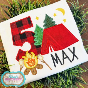 K&ouml;nnte beinhalten: Wei&szlig;es T-Shirt mit Camping-Motiv. Mit einer rot-schwarz karierten Zahl 5, einem roten Zelt, gr&uuml;nen B&auml;umen, einem Lagerfeuer mit Marshmallows und dem Namen "MAX" in Schwarz. Enth&auml;lt Sterne und einen Mond.