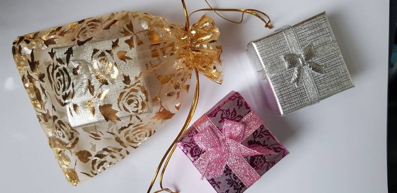 May include: Three gift boxes, one in a gold and white floral pattern, one in a silver and white patterned design, and one in a pink and white floral pattern with a pink ribbon.
