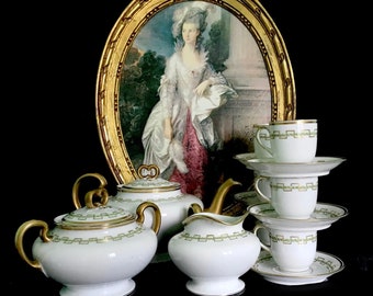 May include: A vintage porcelain tea set with a green and gold trim. The set includes a teapot, creamer, sugar bowl, and two teacups and saucers.