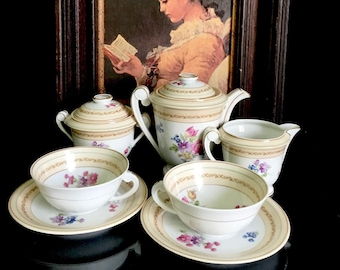 May include: A vintage porcelain tea set with floral designs. The set includes a teapot, creamer, sugar bowl, two teacups, and two saucers. The teacups and saucers have a gold trim and floral patterns.