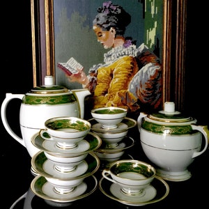 May include: A vintage tea set with a white background, green and gold trim, and a floral design. The set includes a teapot, sugar bowl, creamer, and four cups and saucers.