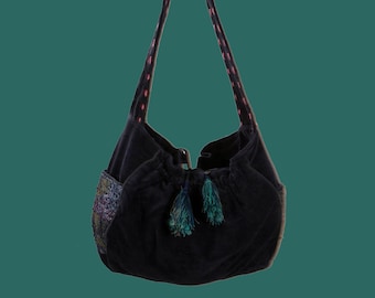 Pode incluir: Uma bolsa azul escura com cordão de ajuste, com costuras cor-de-rosa nas alças e um pequeno remendo bordado na lateral. A bolsa tem duas borlas verdes.