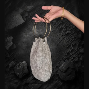Puede incluir: Una bolsa de cordón de plata brillante con dos anillos dorados para asas.