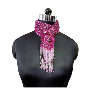May include: A pink sequined scarf with a fringe trim. The scarf is tied around a black mannequin's neck.