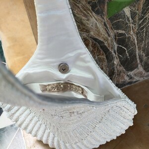 May include: A white beaded evening bag with a satin lining and a metal clasp. The bag is shaped like a seashell and has a long strap.