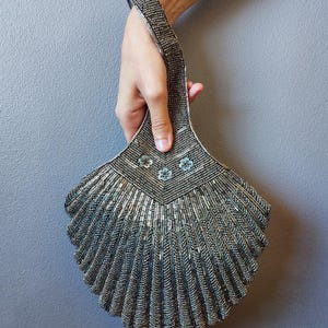 May include: A silver beaded fan-shaped wristlet with a beaded handle and a silver and blue floral design. The wristlet is large and has a grey pearl and gunmetal finish.