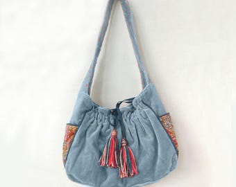 Pode incluir: Bolsa de ombro de veludo azul claro com fecho de cordão e duas borlas decorativas. A bolsa apresenta bolsos de tecido estampado e uma alça a condizer com costuras vermelhas. O texto "Grey with Pink Colour" é visível na parte inferior.