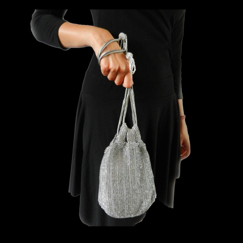 K&ouml;nnte beinhalten: Eine silberne Mesh-Abendtasche mit Kordelzug und Kettenhenkel.