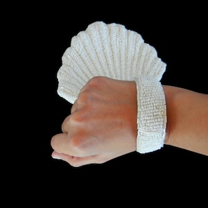 May include: A white beaded bracelet with a shell-shaped design. The bracelet is made of small, white beads that are strung together to create a delicate and elegant look.