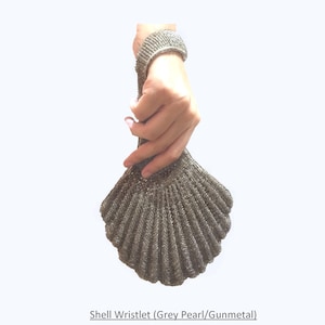 May include: A silver shell-shaped wristlet purse with a grey pearl finish. The wristlet is made of a woven material and has a clasp closure.
