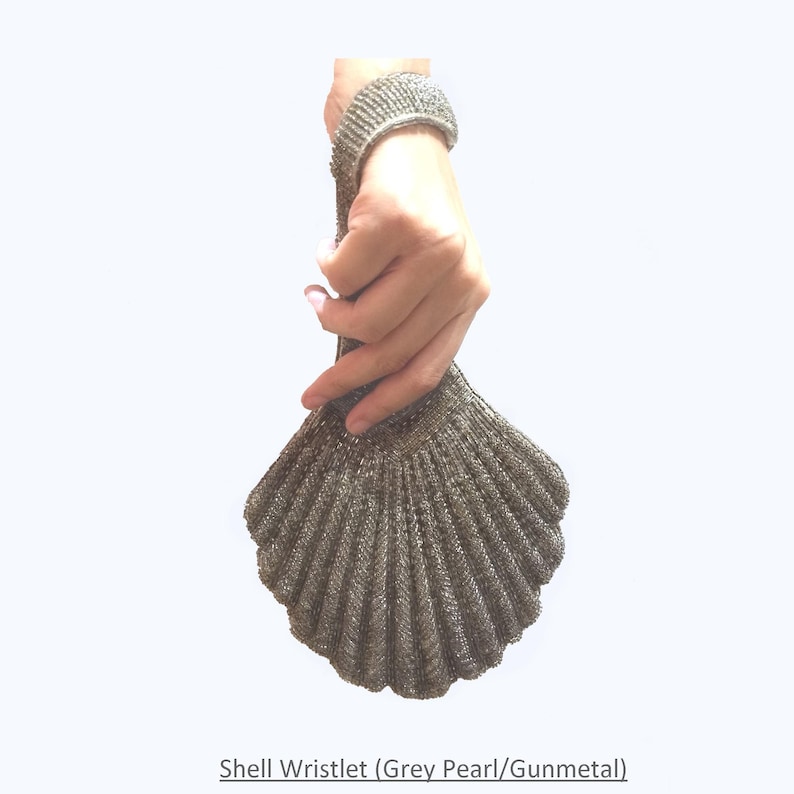 May include: A silver shell-shaped wristlet purse with a grey pearl finish. The wristlet is made of a woven material and has a clasp closure.