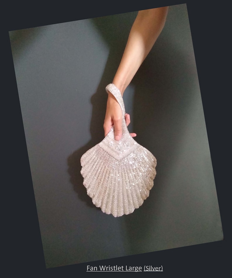May include: A silver beaded fan-shaped wristlet clutch. The wristlet is made of small, shiny beads and has a fan-like shape.
