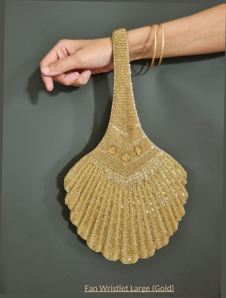 May include: A gold beaded fan-shaped wristlet purse. The purse has a long handle and a fan-shaped design.