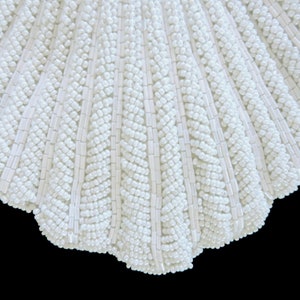 May include: A white beaded seashell-shaped clutch bag. The bag is made of small white beads sewn together in a pattern that resembles a seashell.