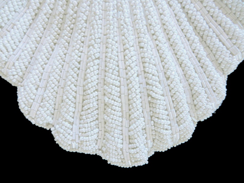 May include: A white beaded seashell-shaped clutch bag. The bag is made of small white beads sewn together in a pattern that resembles a seashell.