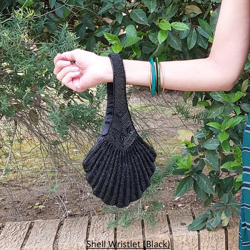 May include: A black beaded shell-shaped wristlet purse. The purse has a beaded strap and a black satin lining.