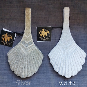 May include: Two beaded purses in the shape of a scallop shell. The purse on the left is silver and the purse on the right is white.