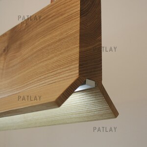 May include: A wooden light fixture with a triangular shape and a light source on the bottom. The fixture is made of light brown wood with a natural grain pattern.