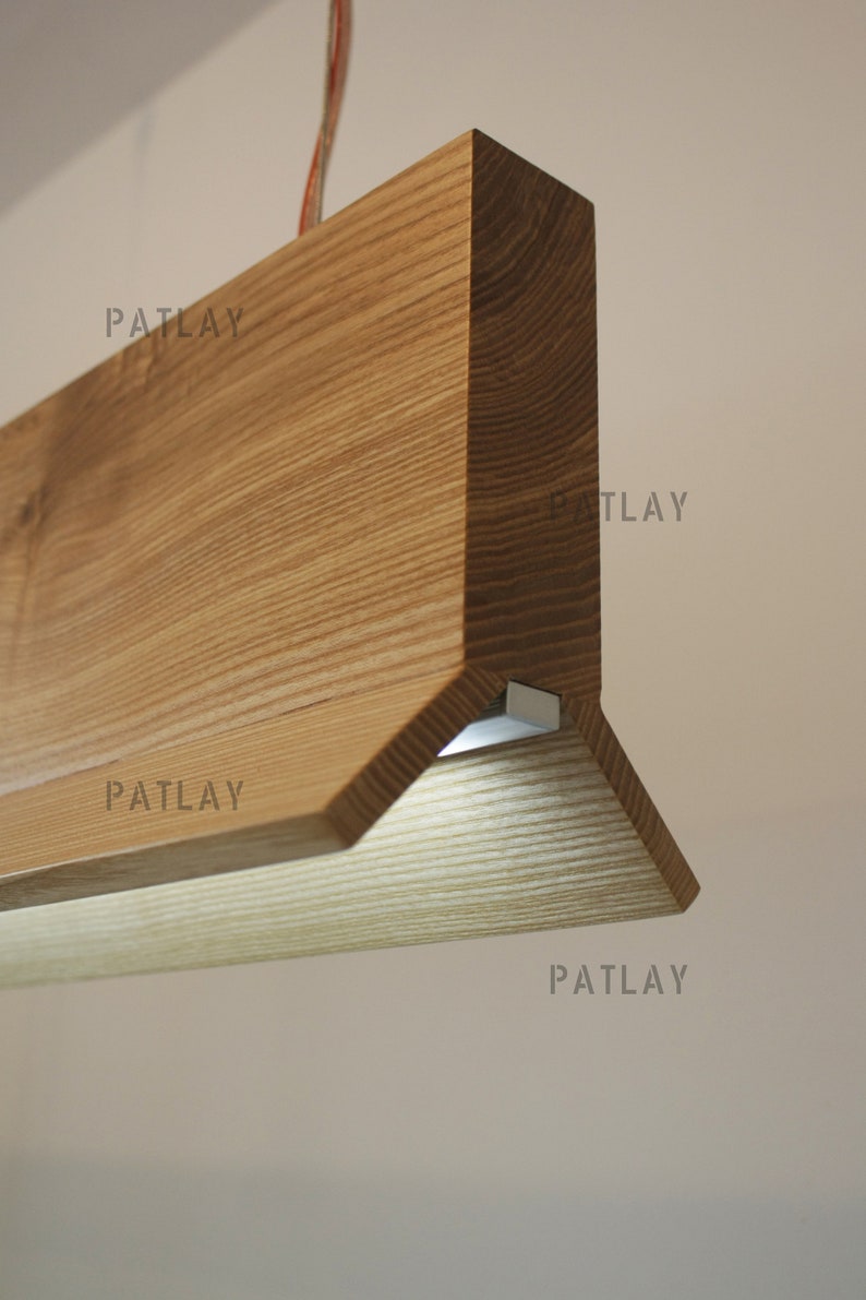 May include: A wooden light fixture with a triangular shape and a light source on the bottom. The fixture is made of light brown wood with a natural grain pattern.