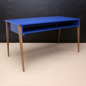 Op de afbeelding: Een blauw bureau met een rechthoekig blad en een onderste plank. Het bureau heeft vier houten poten. Het bureau is geschilderd in een levendige blauwe kleur en de poten hebben een natuurlijke houttint.