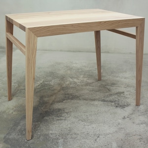 Puede incluir: Una mesa cuadrada de madera con un acabado natural claro. La mesa tiene un diseño sencillo con cuatro patas cónicas y un marco de soporte. La encimera mide aproximadamente 76 cm cuadrados.