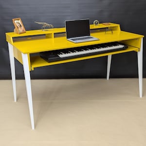 May include: A bright yellow desk with white legs, featuring a pull-out keyboard tray. A laptop sits on the top surface, along with decorative items. The desk is designed for a music studio or home office.