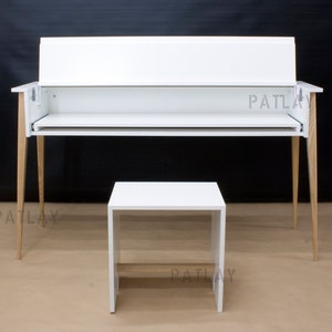 May include: A white desk with a matching white stool. The desk has a rectangular top with a raised back and a pull-out shelf. The legs are made of light-colored wood. The stool is a simple cube shape. The text "PATLAY" is visible.
