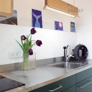 May include: A modern kitchen with dark green cabinets and stainless steel countertops. A wooden light fixture hangs above the sink. There are three framed pictures on the wall behind the sink. A vase of purple tulips sits on the counter.