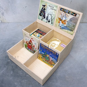 May include: A wooden box with five compartments, each holding a different children's book. The books have colorful covers with illustrations and Russian text. The box is open and the books are visible.