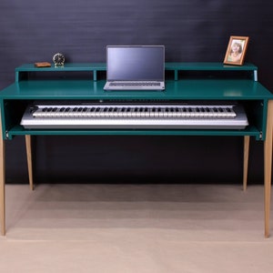 May include: A teal green desk with a keyboard drawer and a laptop on the top surface. The desk has light wood legs and a small shelf above the keyboard drawer.