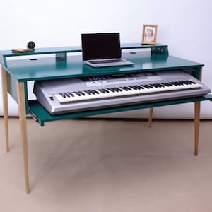May include: A teal green desk with a pull-out keyboard tray. The desk has a light wood base and a small shelf above the keyboard tray. A laptop computer is on the desk.