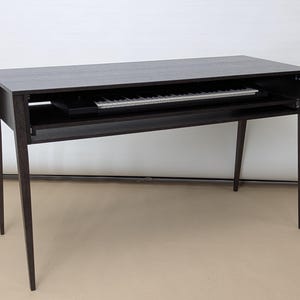 May include: A black wooden desk with a pull-out shelf for a keyboard. The desk has a simple design with four legs.