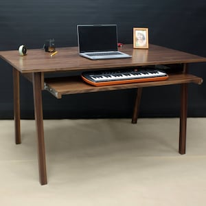 Może przedstawiać: Biurko z drewna orzechowego z wysuwaną szufladą na klawiaturę. Na biurku znajduje się laptop, ołówek, mały zegar i ramka na zdjęcie. Na wysuwanej szufladzie znajduje się pomarańczowa klawiatura.