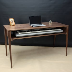 Könnte beinhalten: Ein Schreibtisch aus Walnussholz mit einer ausziehbaren Tastaturablage. Ein Laptop, ein Bilderrahmen und eine Uhr stehen auf dem Schreibtisch.