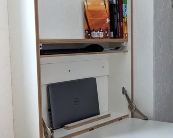 May include: White wall-mounted desk with a fold-down top and a shelf above. A laptop computer is on the desk, and a few books are on the shelf. The desk is made of plywood and has silver hinges.