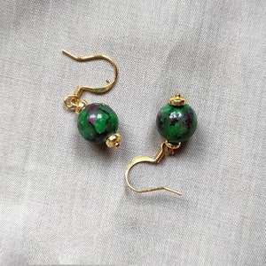 Puede incluir: Un par de pendientes de oro con cuentas de piedras preciosas verdes y moradas.