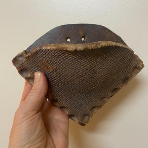 May include: A small, brown, ceramic planter with a textured surface and two holes on the top. The planter is shaped like a triangle with rounded edges.