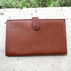May include: A rectangular, brown leather wallet with a flap closure. The wallet is a warm, medium brown color and appears to be made of genuine leather. The flap is secured with a matching leather tab. The wallet is likely designed to hold cards and cash.