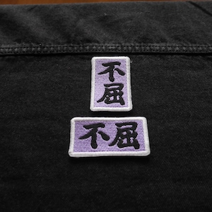 K&ouml;nnte beinhalten: Zwei violette gestickte Patches mit den chinesischen Schriftzeichen "不屈" (bedeutet "unbeugsam") in Schwarz.