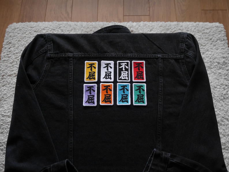 K&ouml;nnte beinhalten: Schwarze Jeansjacke mit acht gestickten Patches. Jeder Patch zeigt die chinesischen Schriftzeichen "不" und "風" in verschiedenen Farben, darunter Orange, Gelb, Rot, Gr&uuml;n, Blau, Lila und Wei&szlig;.